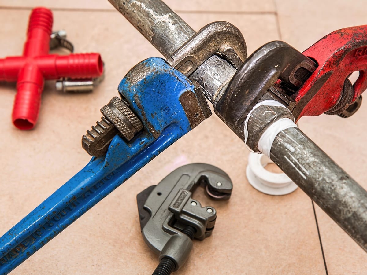 Pipe wrenches gripping a galvanized pipe alongside a pipe cutter and fittings