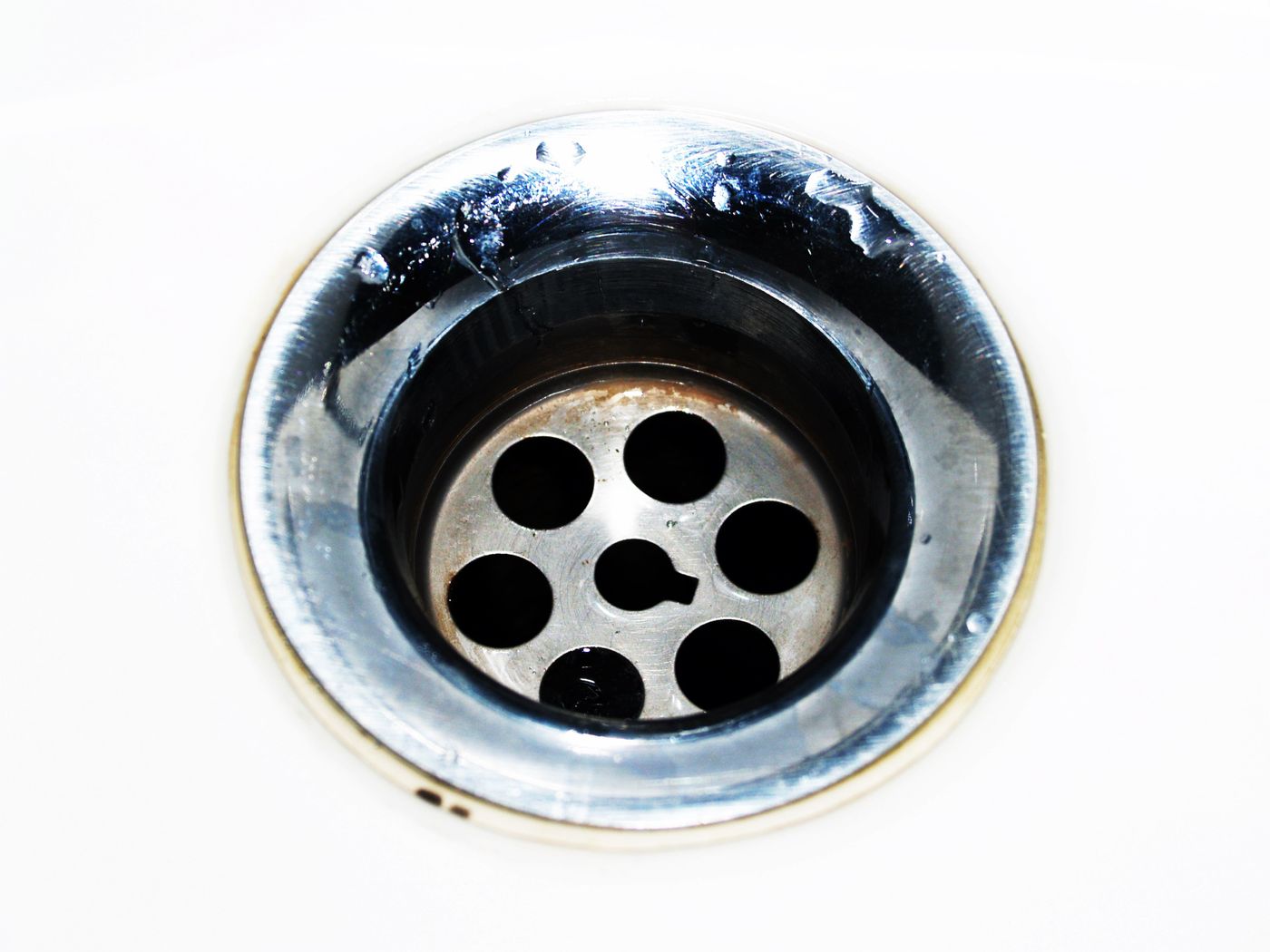 Close-up of a stainless steel sink drain with a perforated strainer and water and grime around the opening