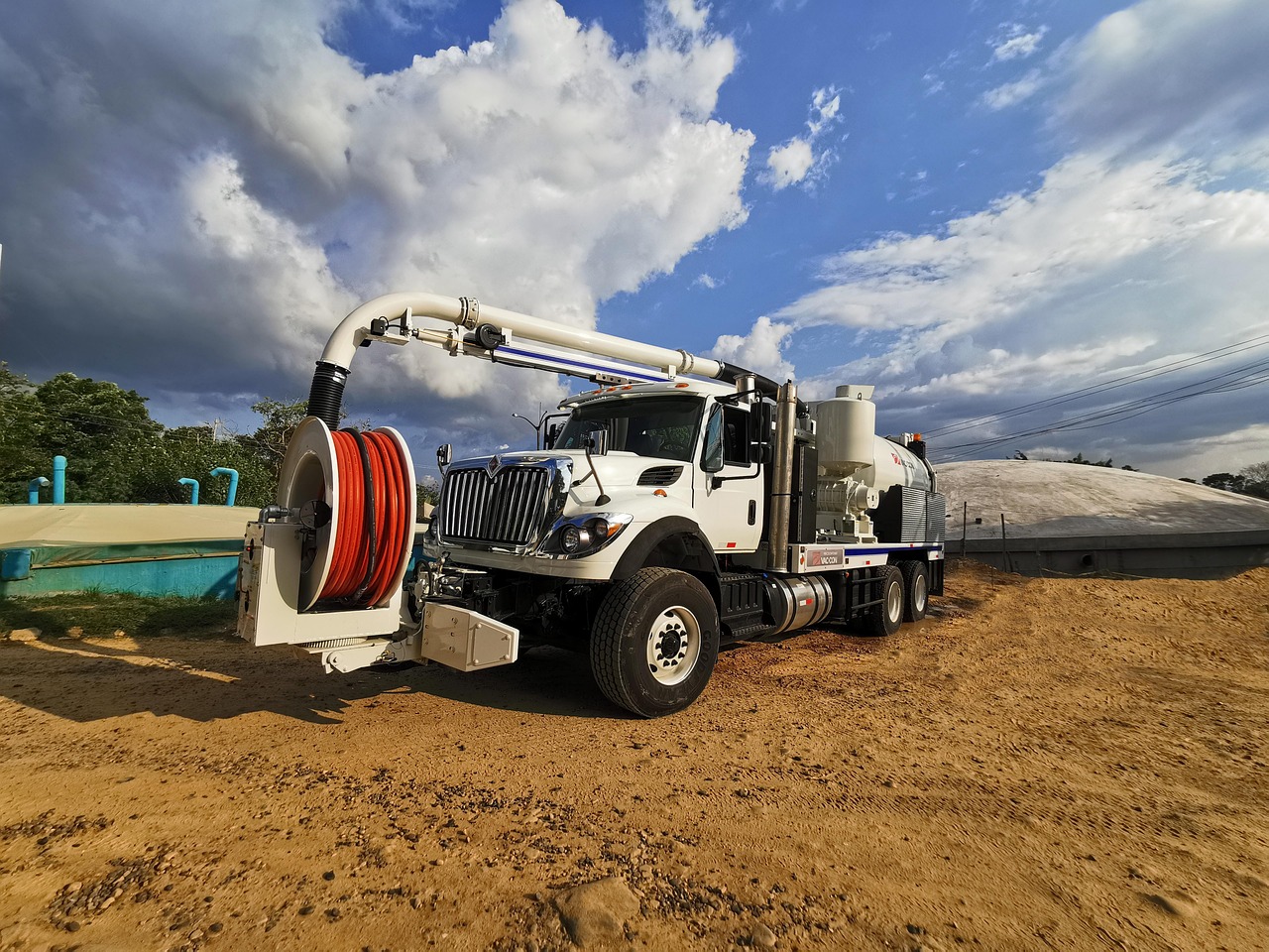 A sewer and drain cleaning vacuum jetter truck with a large hose reel parked at a worksite