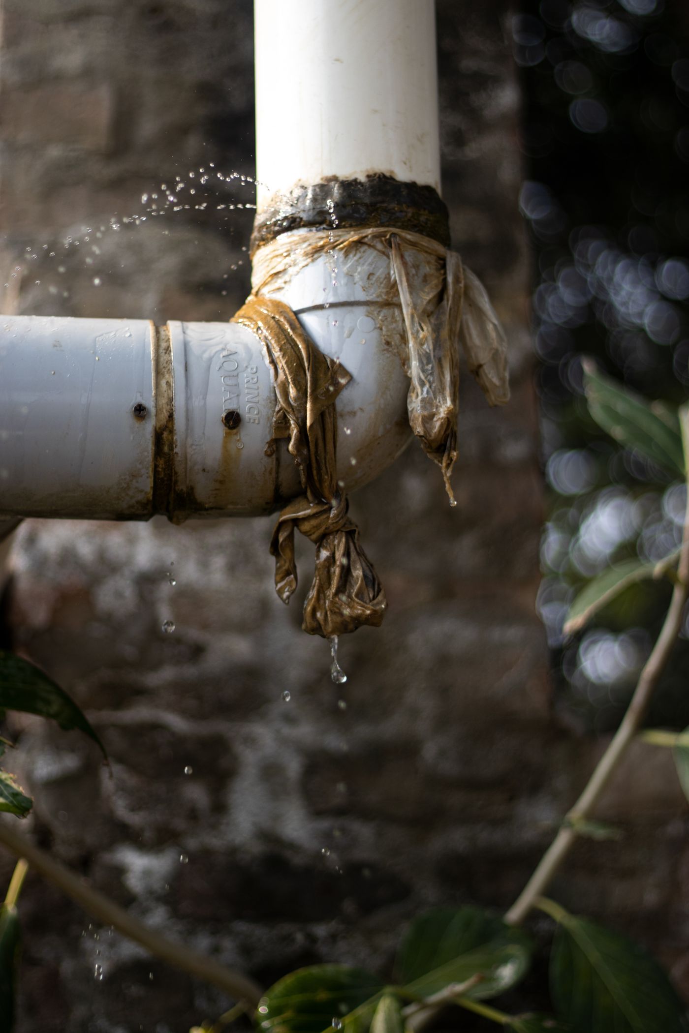 Leaking PVC pipe joint spraying water, crudely patched with plastic and tape