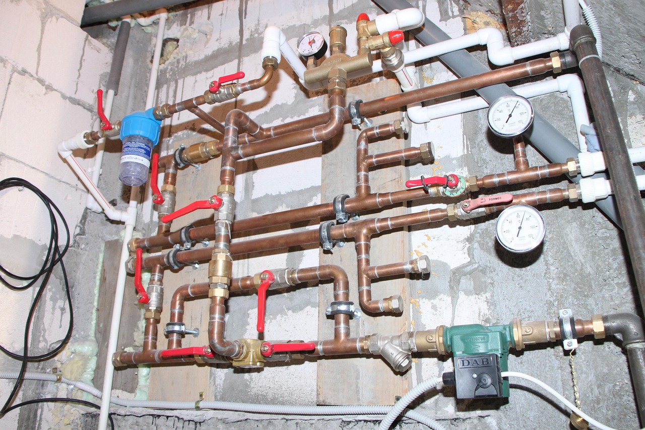 Indoor copper plumbing with red-handled water shut-off valves and pressure gauges mounted on a wall