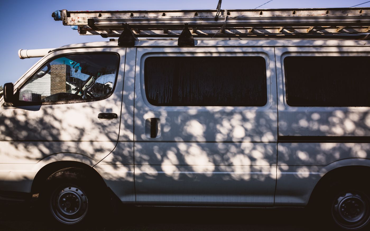 White work service van with a ladder rack on the roof parked under tree shade