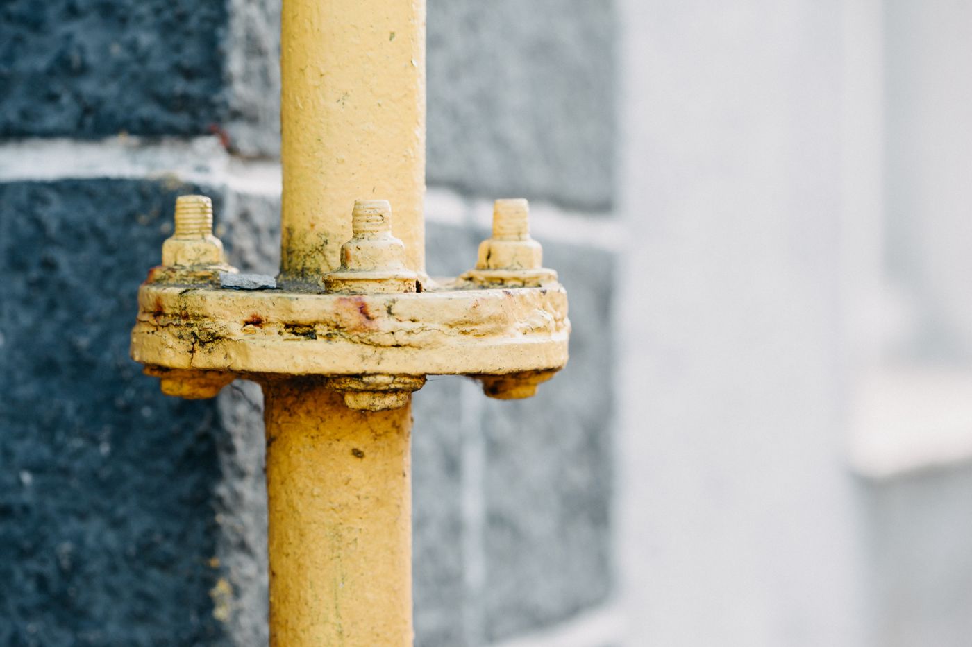 Close-up of a yellow gas pipe with a bolted flange connection against a stone wall