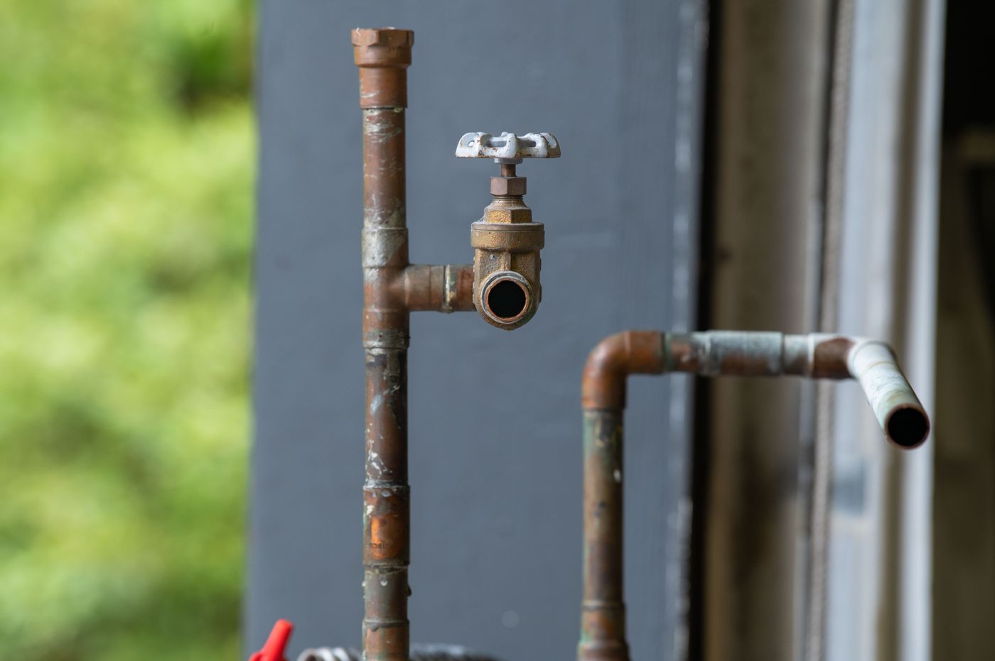 Aged copper water supply pipes and a brass shutoff valve showing surface corrosion and oxidation