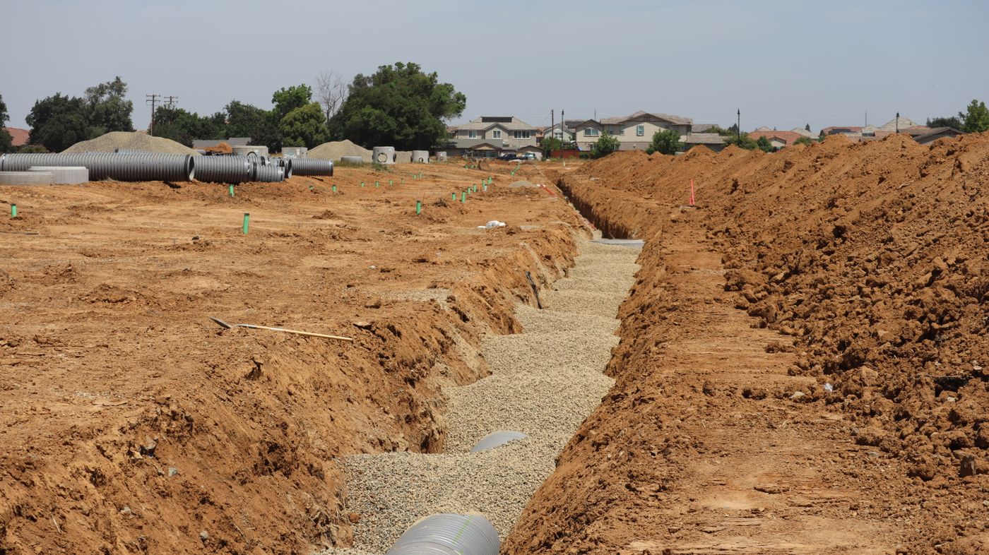 A residential sewer line laid in an open trench, with houses in the background