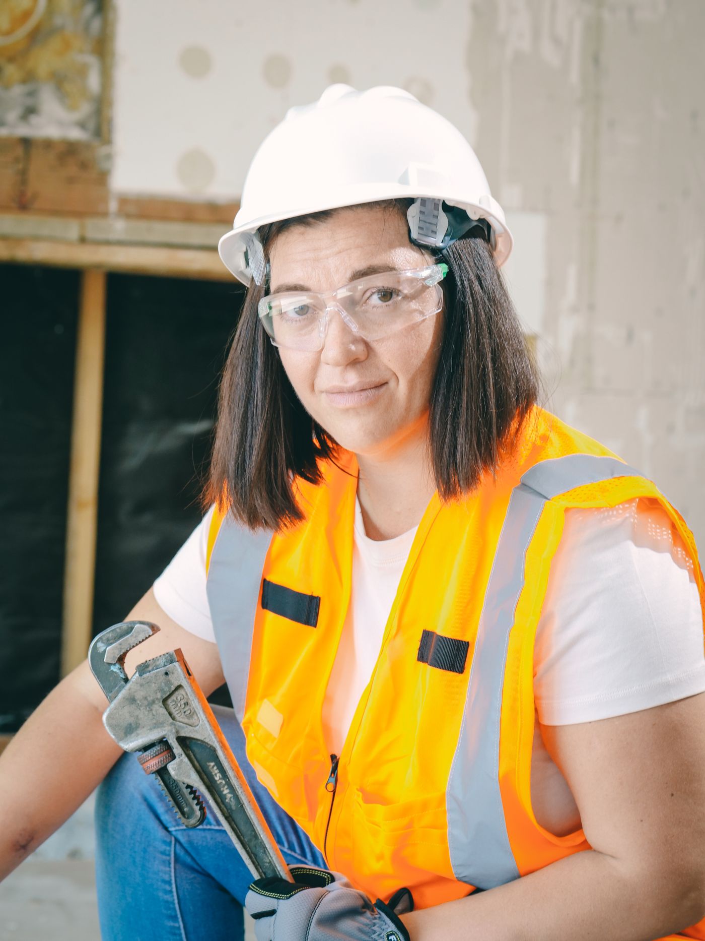 A plumber in safety gear holding a pipe wrench on a job site