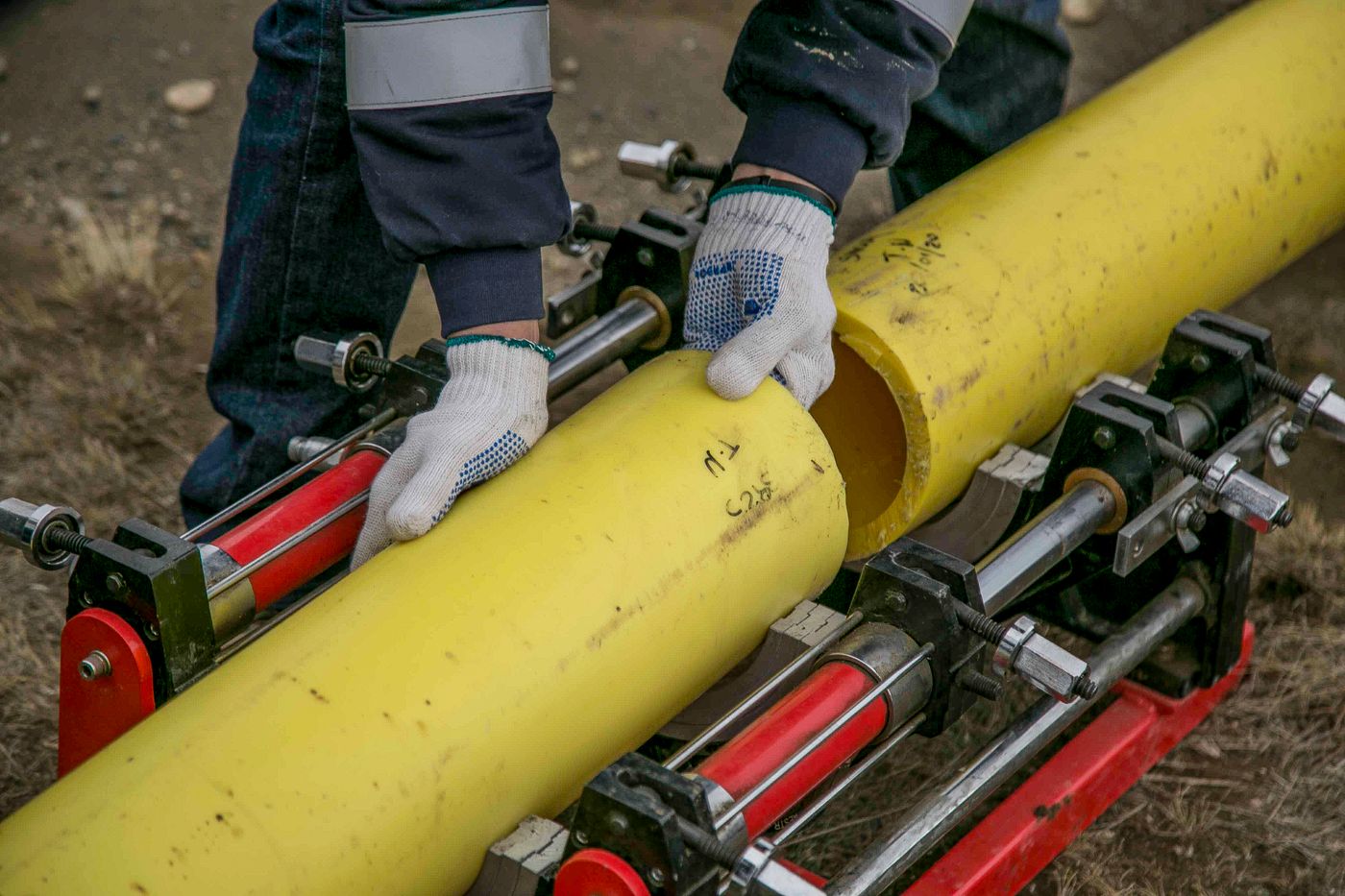 Gloved hands joining a new section of pipe with alignment clamps