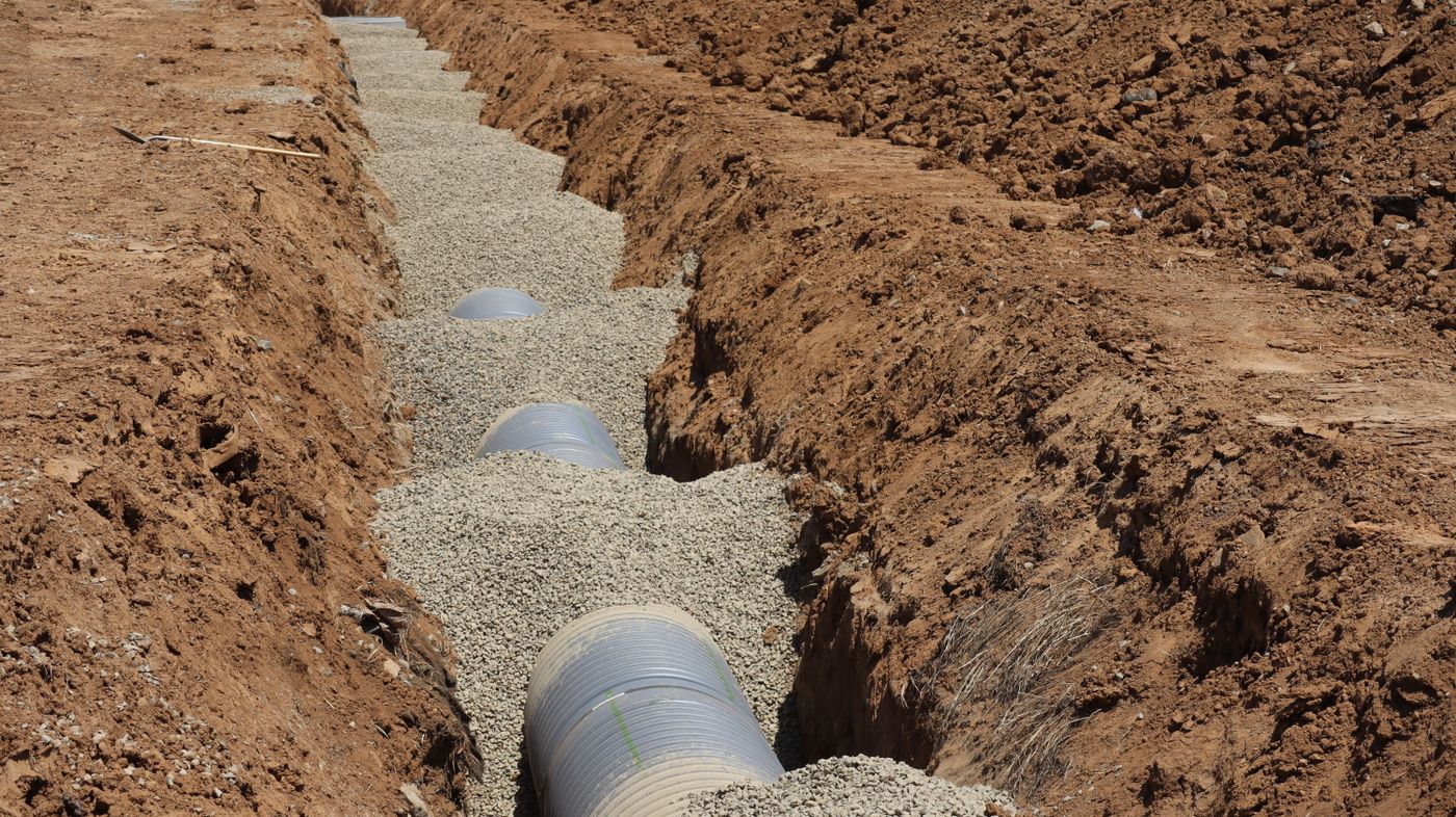 A drainage pipe bedded in gravel inside an open excavation trench