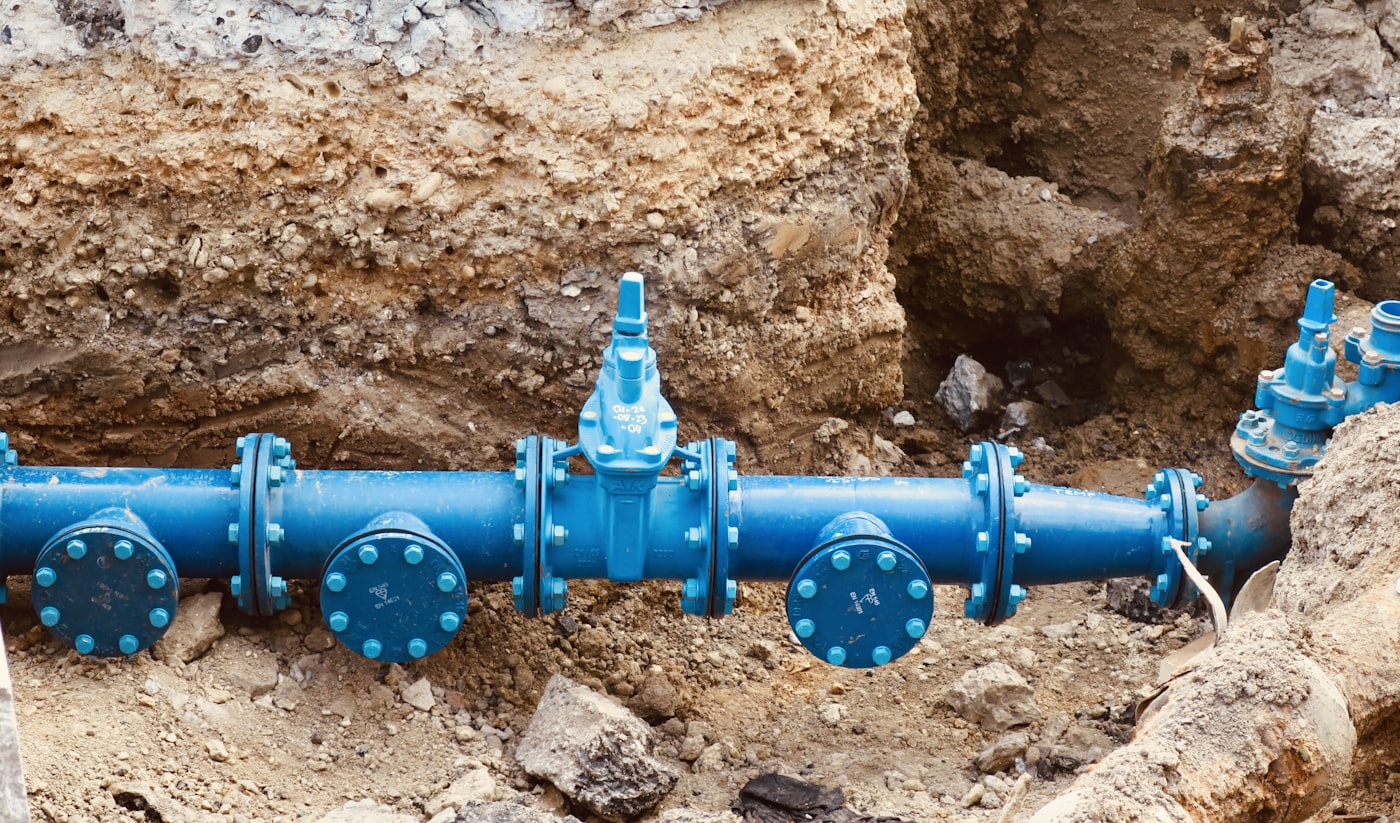 Blue ductile sewer and water main pipes with gate valves sitting in an excavated earth pit