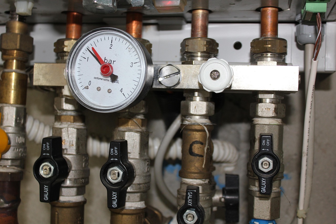 Close-up of a water heater pipe manifold with a pressure gauge and isolation valves during servicing